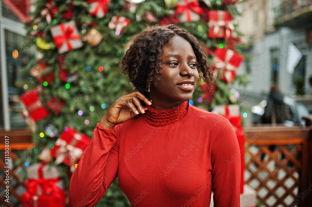 Portrait of a curly haired african woman wearing fashionable red turtleneck posing against christmas decorations, new year eve theme. Portrait of a curly haired african woman wearing fashionable red turtleneck posing against christmas decorations, new year eve theme.