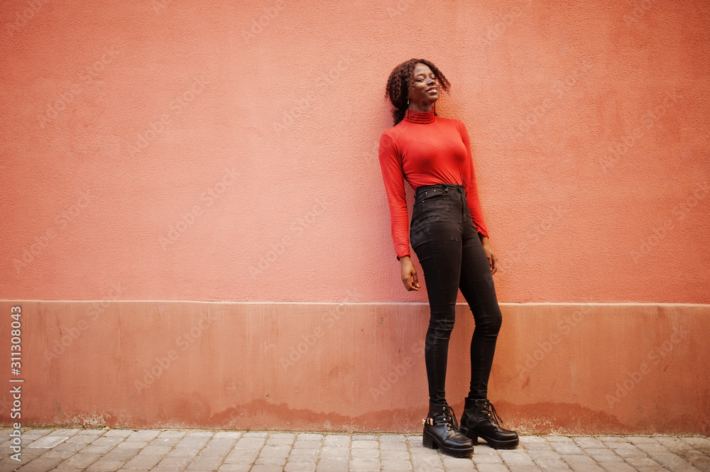 Portrait of a curly haired african woman wearing fashionable red turtleneck posing against rose wall. Portrait of a curly haired african woman wearing fashionable red turtleneck posing against rose wall.