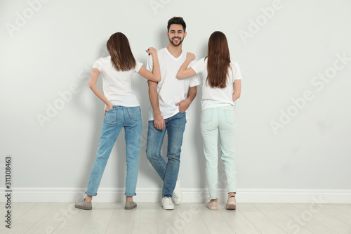 Group of young people in stylish jeans near light wall