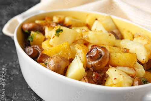 Baking dish with tasty cooked mushrooms and potato on dark background, closeup