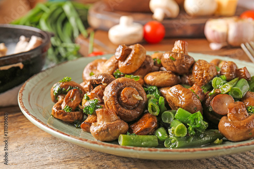 Plate with tasty cooked mushrooms and green beans on table, closeup