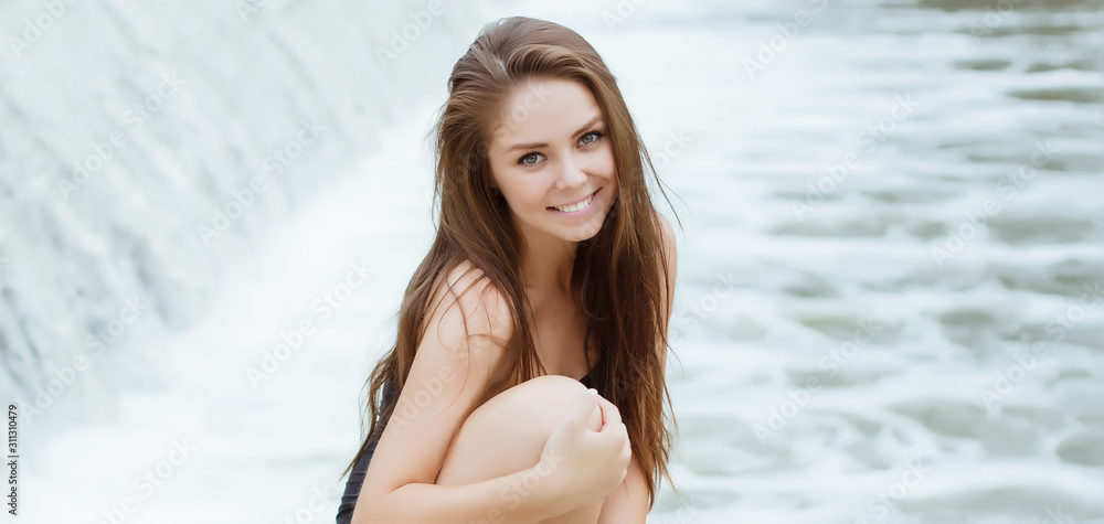 Young beautiful woman with perfect smile and white teeth against the background of the waterfall Young beautiful woman with perfect smile and white teeth against the background of the waterfall