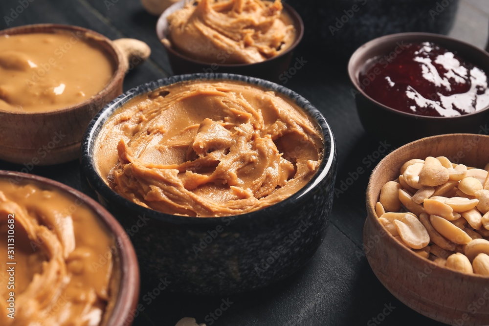 Bowls with tasty peanut butter and jam on dark table