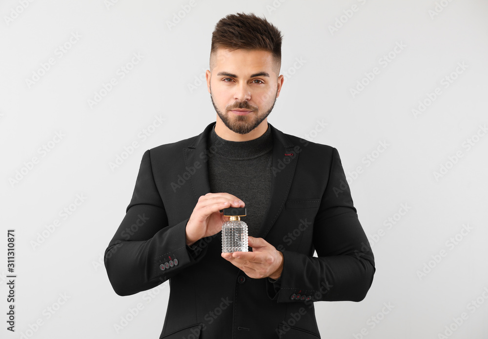 Handsome young man with bottle of perfume on light background Handsome young man with bottle of perfume on light background