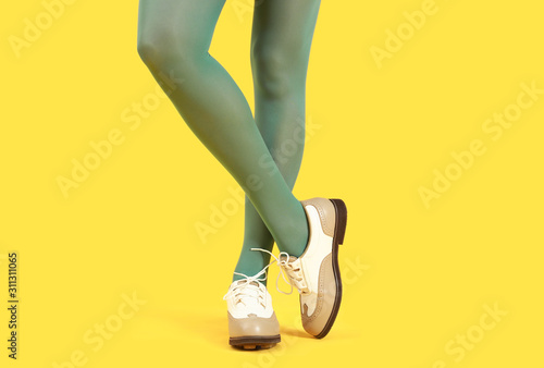 Legs of young woman in stylish shoes and tights on color background