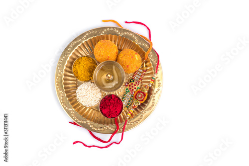 Indian Festival: Rakhi with rice grains, kumkum, sweets and diya on plate with an elegant Rakhi. A traditional Indian wrist band which is a symbol of love between Brothers and Sisters