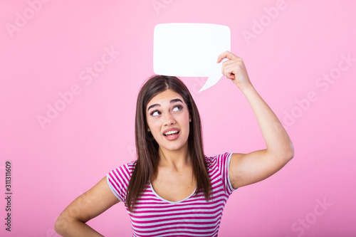 Hey, great idea. Happy pensive beautiful girl looking at blank speech bubble, copy space. Beautiful young joyful model on pink background having idea. photo