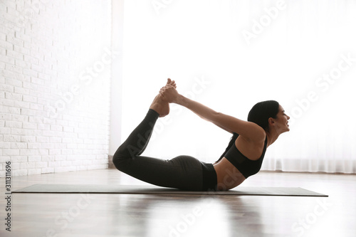 Young woman practicing bow asana in yoga studio. Dhanurasana pose