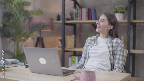 Confident Caucasian businesswoman typing on laptop, reclining on chair, and smiling. Successful female freelancer working distantly from home. Freelance, professional occupation, happiness. photo