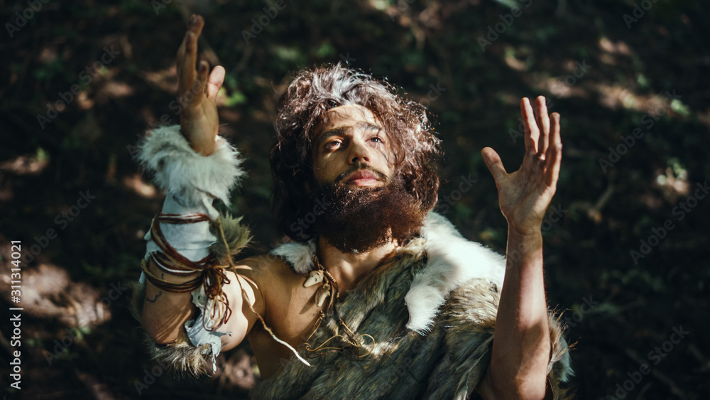 Portrait of Primeval Caveman Wearing Animal Skin Raises Hands to Heaven Looking at the Sun, Having Pagan Religious Experience. Prehistoric Neanderthal Believing and Praying to God. High Angle Shot 