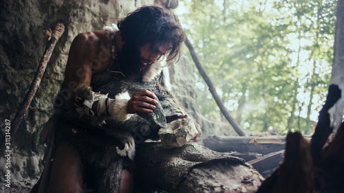 Photos Primeval Caveman Wearing Animal Skin Hits Rock with Sharp Stone and Makes First Primitive Tool for Hunting Animal Prey or to Handle Hides