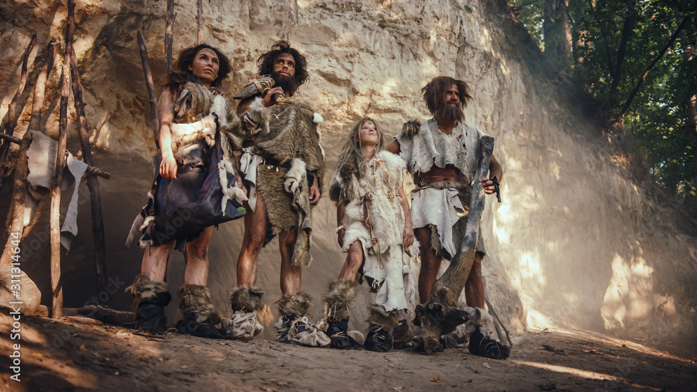Tribe of Four Hunter-Gatherers Wearing Animal Skin Holding Stone Tipped Tools, Pose at the Entrance of their Cave. Portrait of Two Grown Male and Two Female Neanderthals and their Way of Living Tribe of Four Hunter-Gatherers Wearing Animal Skin Holding Stone Tipped Tools, Pose at the Entrance of their Cave. Portrait of Two Grown Male and Two Female Neanderthals and their Way of Living