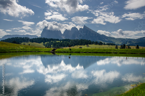 Reflection of Sassolungo and Langkofel mountain group and cloudy blue sky in lake, Picturesque. Alpe di Siusi or Seiser Alm with Sassolungo and Langkofel mountain group, South Tyrol, Italy