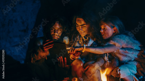 Tribe of Prehistoric  Primitive Hunter-Gatherers Wearing Animal Skins Use Digital Tablet Computer in a Cave at Night. Neanderthal or Homo Sapiens Family Browsing Internet  Watching Videos  TV Shows 