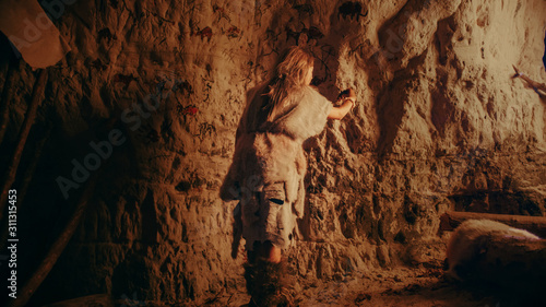 Foto Back View of a Primitive Prehistoric Neanderthal Child Wearing Animal Skin Draws Animals and Abstracts on the Walls at Night