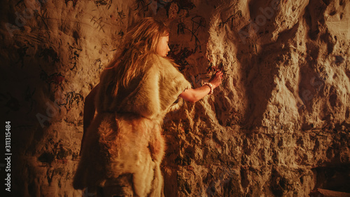 Foto Back View of a Primitive Prehistoric Neanderthal Child in Animal Skin Draws Animals and Abstracts on the Walls at Night