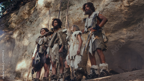 Tribe of Hunter-Gatherers Wearing Animal Skin Holding Stone Tipped Tools, Stand Near Cave Entrance. Neanderthal Family Ready for Hunting in the Jungle or Migration photo