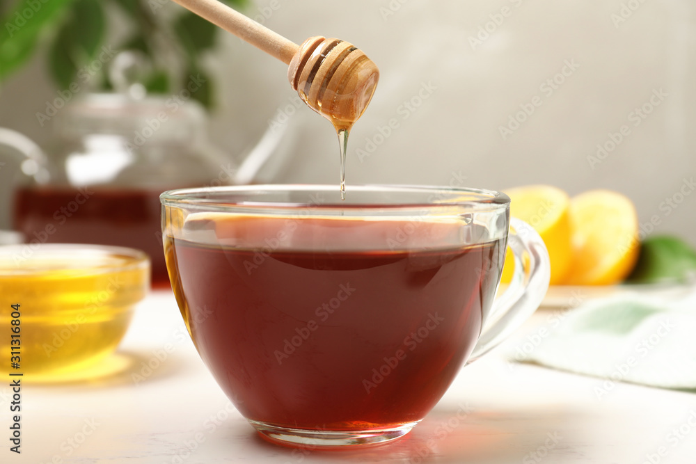 Honey dripping into cup of tea on white table Honey dripping into cup of tea on white table