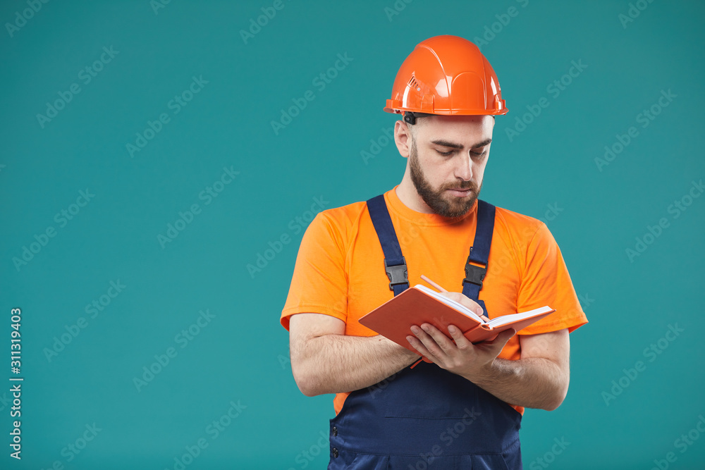 Waist up studio portrait shot of young male laborer wearing uniform writing something in notebook Waist up studio portrait shot of young male laborer wearing uniform writing something in notebook