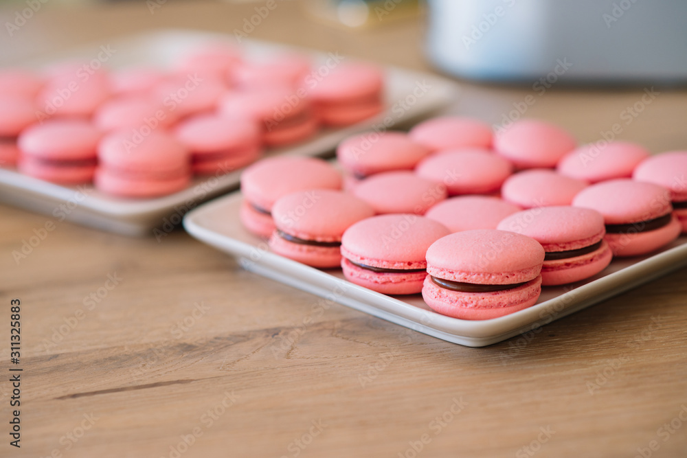 Beautiful pink macaroons with chocolate ganache on a white square plate stand on a wooden table Beautiful pink macaroons with chocolate ganache on a white square plate stand on a wooden table