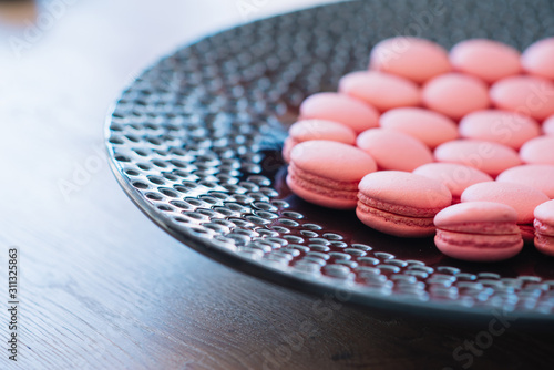 Beautiful pink macaroons lie on a large black plate with a round pattern.