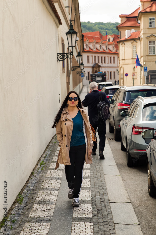 Young Brunette woman walking street.   Narrow streets  with cobblestone pavement in Prague. Medeival architecture. Cars on narrow street.