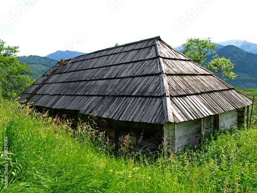 Abandoned and forgotten gutsul house high in green mountains. Picturesque summer mountain landscape in the Eastern Carpathians. An old gutsul wooden architecture in highlands. Village in oblivion photo