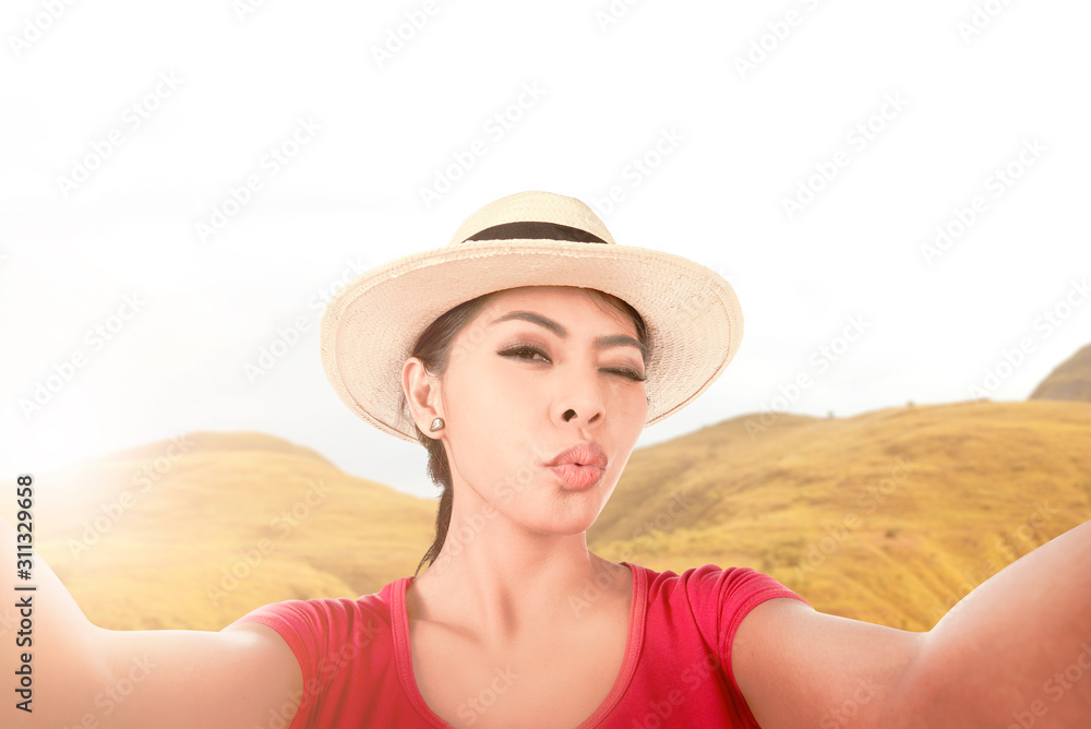 Asian girl in hat making a selfie with a funny face using the camera phone