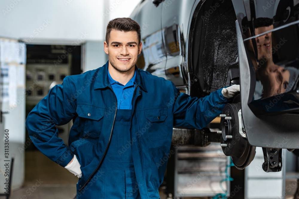 smiling mechanic looking at camera while touching disc brakes of car smiling mechanic looking at camera while touching disc brakes of car