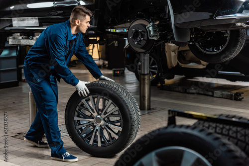 young mechanic holding car wheel near raised car in workshop © LIGHTFIELD STUDIOS