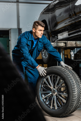 selective focus of young mechanic with car wheel near raised car in workshop © LIGHTFIELD STUDIOS