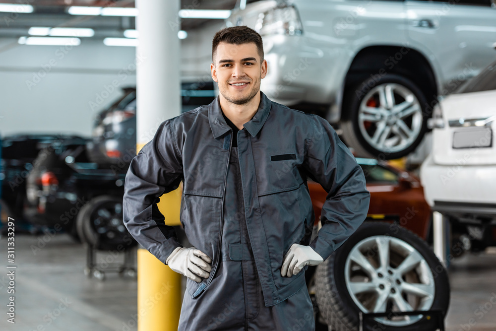smiling mechanic looking at camera while standing in workshop with hands on hips smiling mechanic looking at camera while standing in workshop with hands on hips
