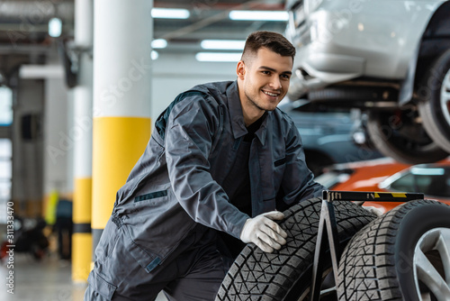 handsome, smiling mechanic holding new tire in workshop