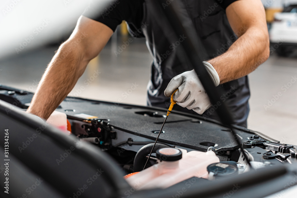 partial view of mechanic checking engine oil level with dipstick