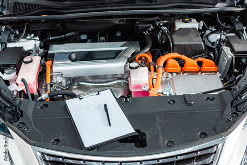 Clipboard with blank white paper and pen near car engine compartment