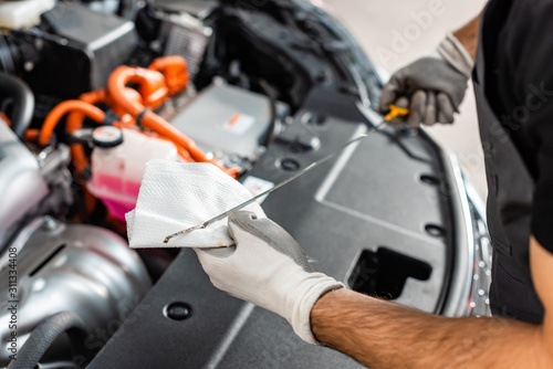 cropped view of mechanic wiping oil dipstick with rag near car engine compartment