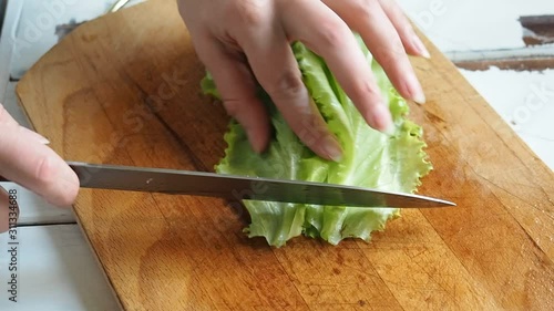 A female chef prepares a healthy salad of fresh vegetables. Vegetarian food. Slicing lettuce leaves on a wooden Board in the home kitchen.