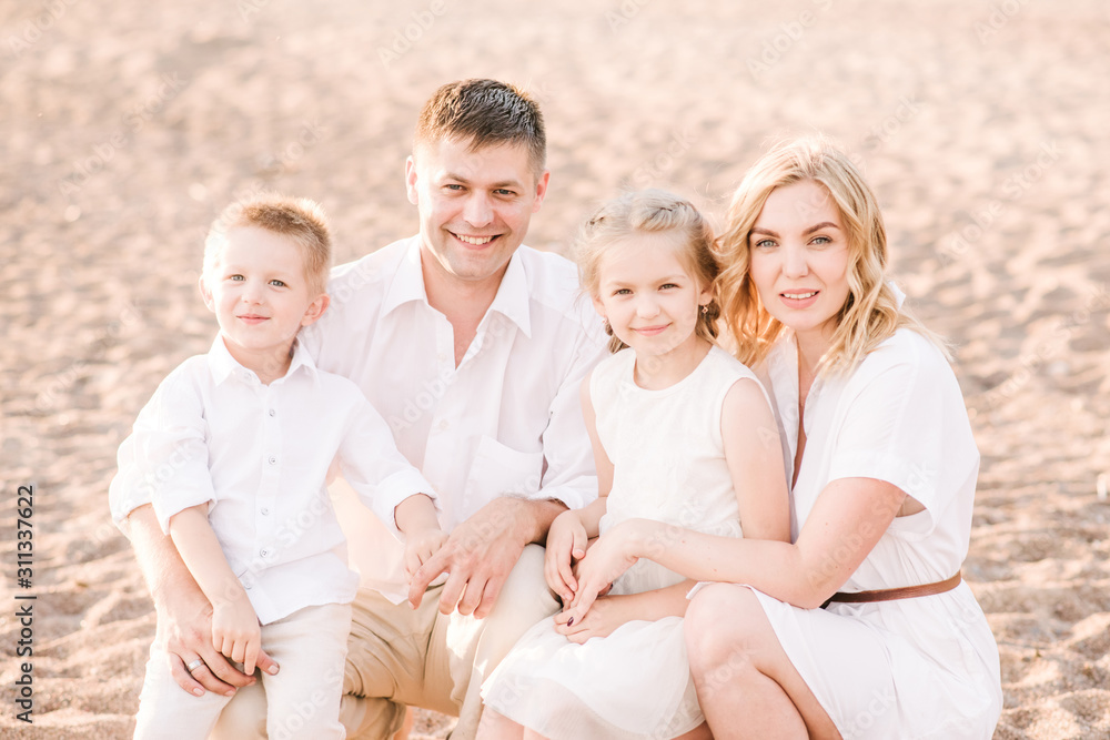 Portrait of white family of four on a beach during sunset. Everyone is