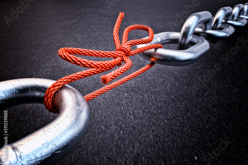 Weakest link, security break fix and strength concept, metallic chain connected by a red knotted rope on black background photo