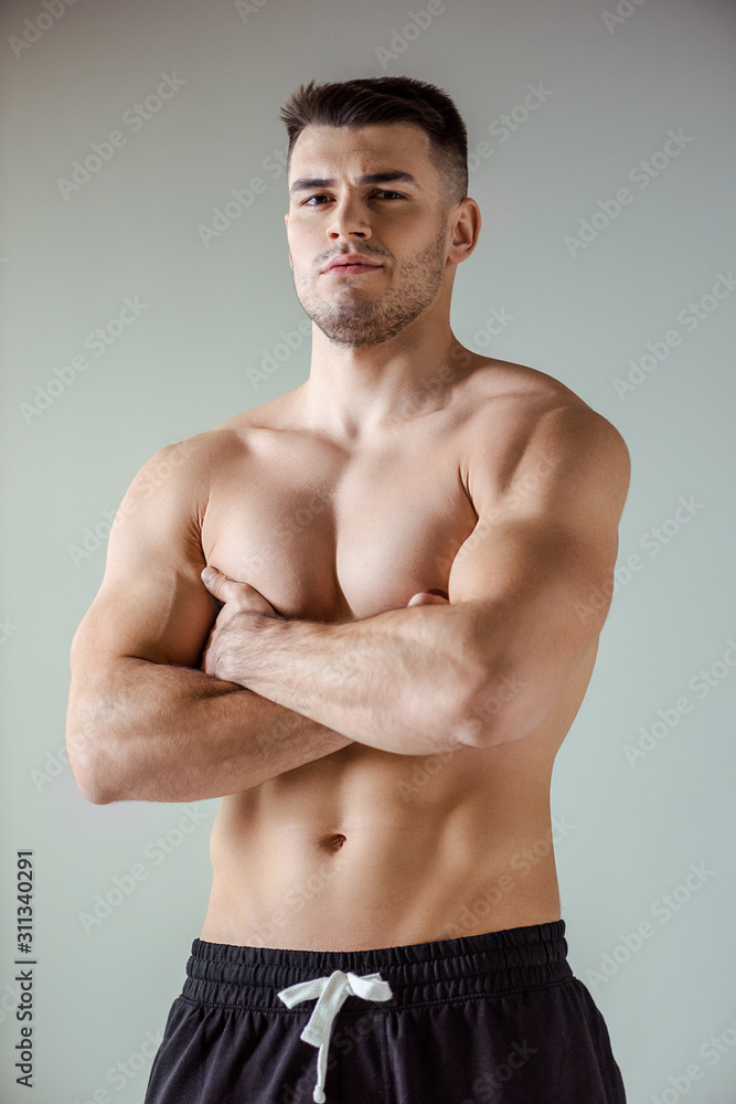 Fototapeta premium sexy muscular bodybuilder with bare torso posing with crossed arms isolated on grey