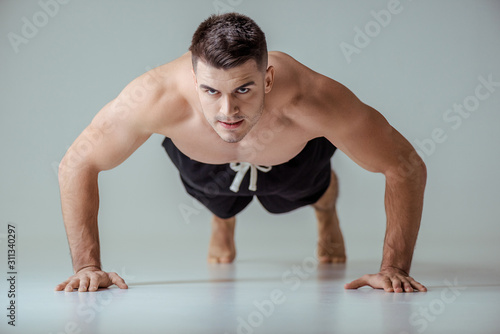 sexy muscular sportsman with bare torso doing push ups on grey