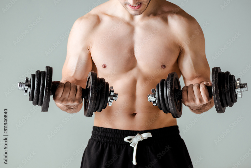 partial view of sexy muscular bodybuilder with bare torso exercising with dumbbells isolated on grey