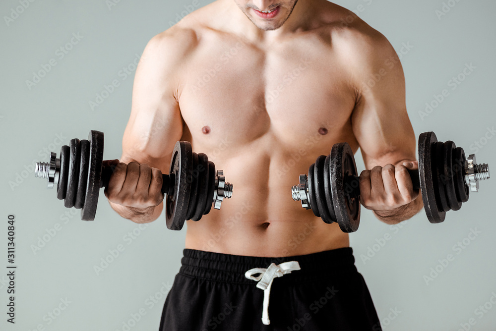 partial view of sexy muscular bodybuilder with bare torso exercising with dumbbells isolated on grey partial view of sexy muscular bodybuilder with bare torso exercising with dumbbells isolated on grey