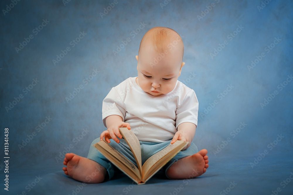 Cute little toddler in light clothes curiously leafs through an old book on a clear blue background. Education concept Cute little toddler in light clothes curiously leafs through an old book on a clear blue background. Education concept