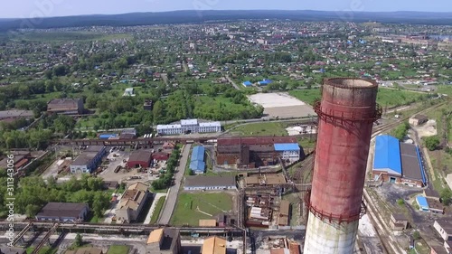 Aerial view of heavy industry buildings near a residential area on a summer day. The drone fired back near the top of the industrial pipe. No smoke comes from the chimney. The metallurgical plant was  photo