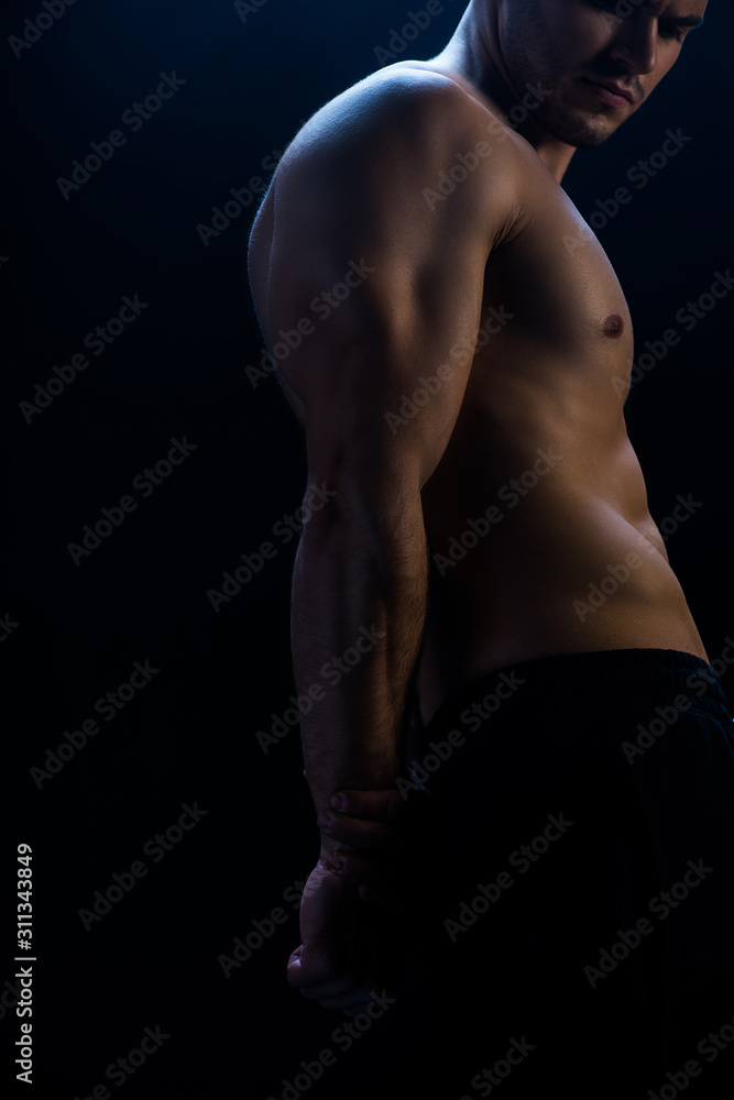 cropped view of sexy muscular bodybuilder with bare torso on black background