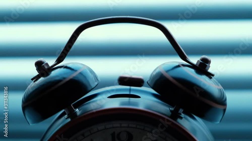 An old vintage alarm clock is ringing, against the background of the blinds.