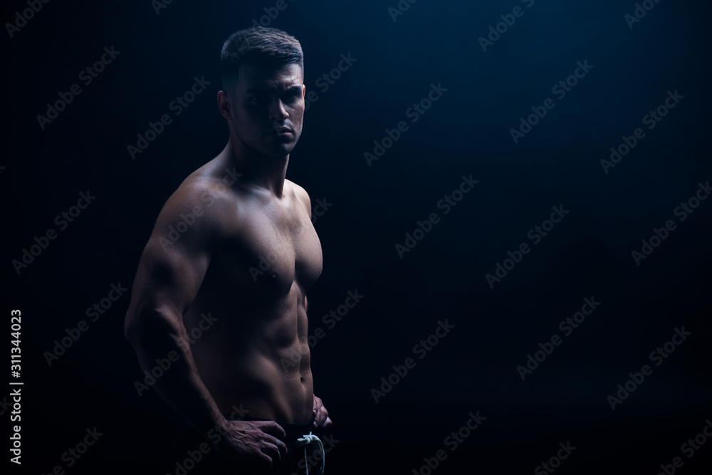 sexy muscular bodybuilder with bare torso posing with hands on hips isolated on black