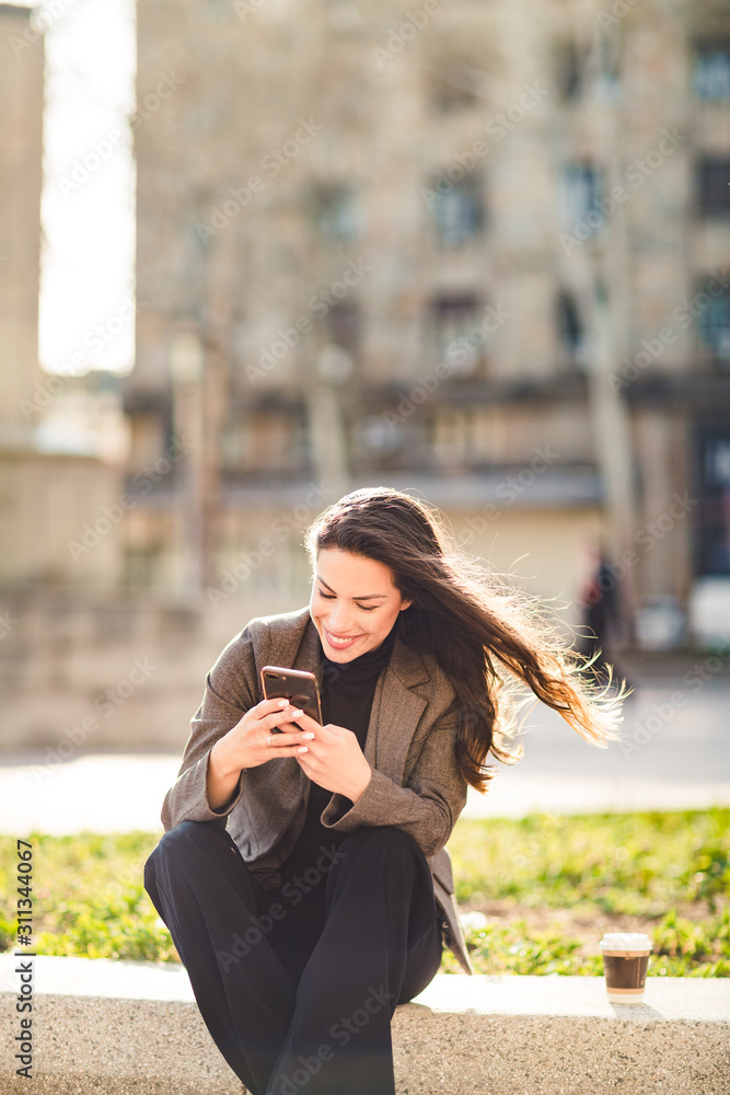 Attractive young woman looking at her smart phone and smiling while sitting Attractive young woman looking at her smart phone and smiling while sitting