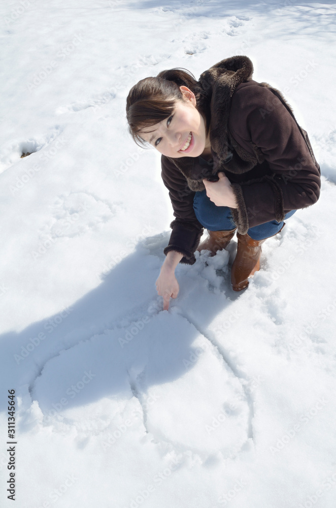 雪にハートを書く女性